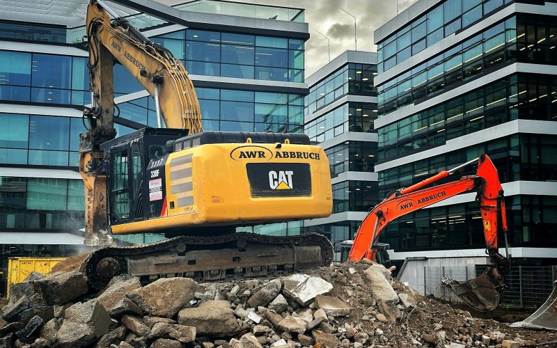 a bulldozer digging through a pile of rubble in front of a building