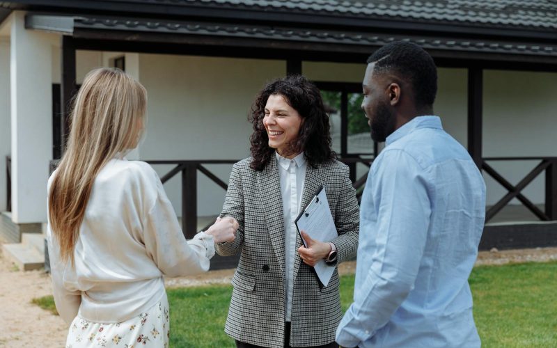 A real estate agent shakes hands with a couple outside a modern house, symbolizing a successful property deal.