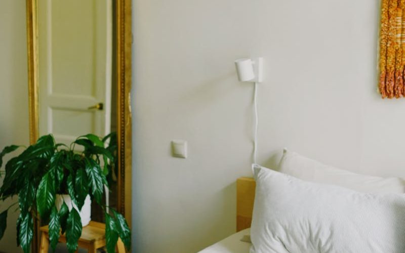 High angle of modern opened laptop with power bank and cup of hot drink placed on comfortable bed with soft blanket and pillows in stylish bedroom in daylight